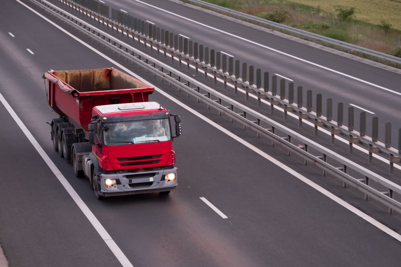 An overhead view of a red dump truck driving on an open highway during the day.