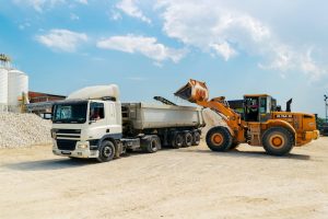 Excavator loading materials into a heavy-duty truck at a sunny construction site.